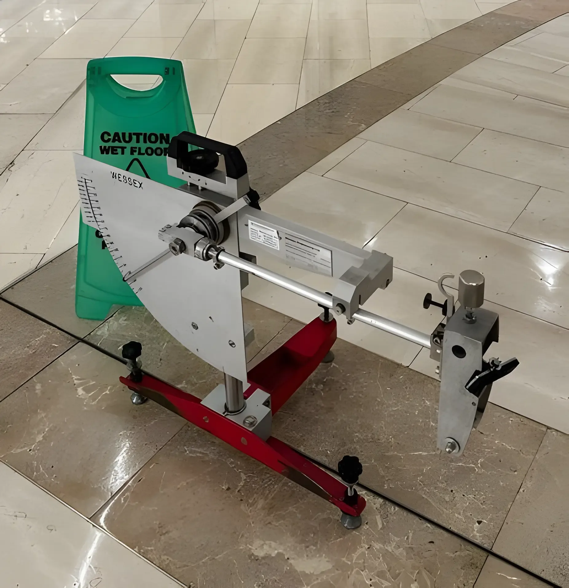 Wet pendulum tester and green caution sign set up on a polished stone tiled floor