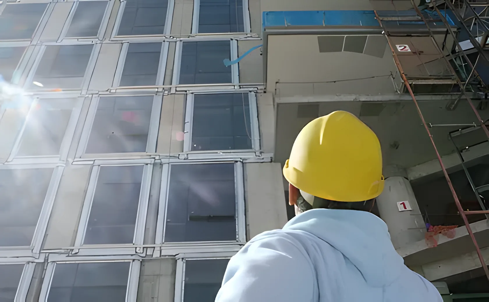 Construction worker in a yellow hard hat inspecting a commercial building under construction