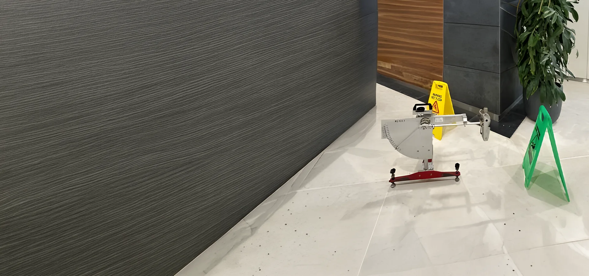 Pendulum slip tester set up beside a wet floor sign on polished stone tiles in a building lobby