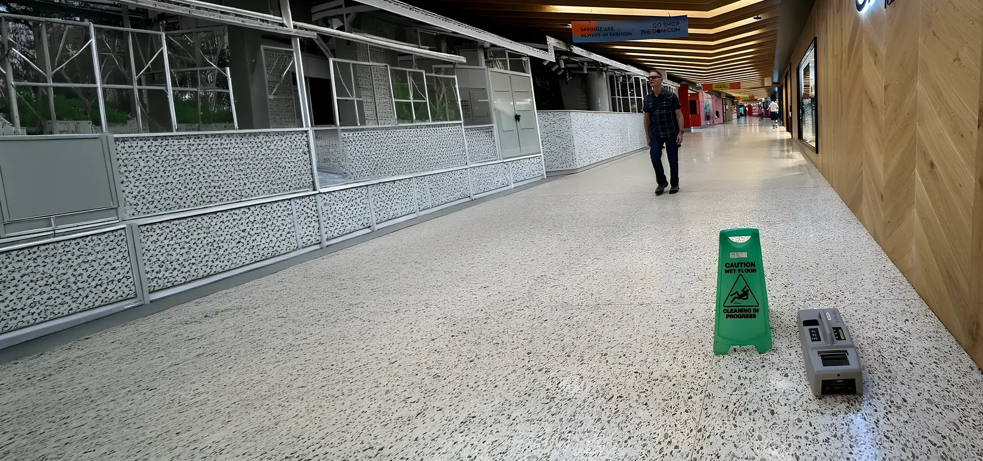 Shopping centre walkway with a green caution wet floor sign and portable slip testing equipment set up for an urgent assessment