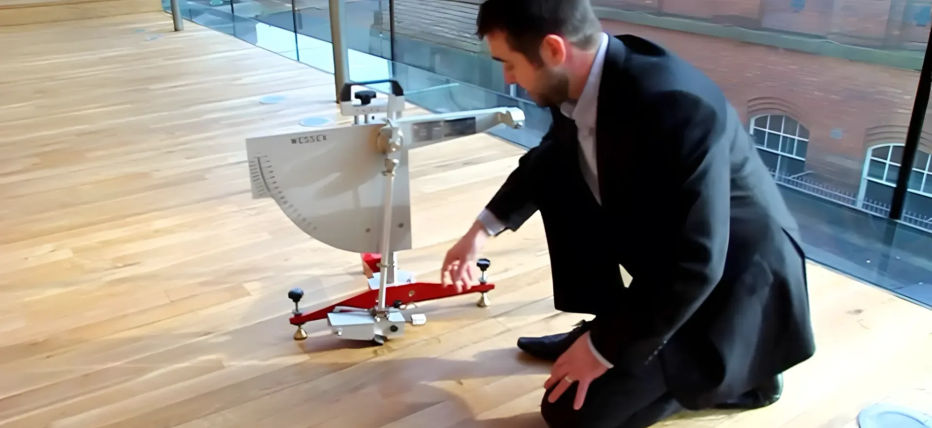 Consultant setting up a wet pendulum slip tester on a timber floor beside a glass balustrade